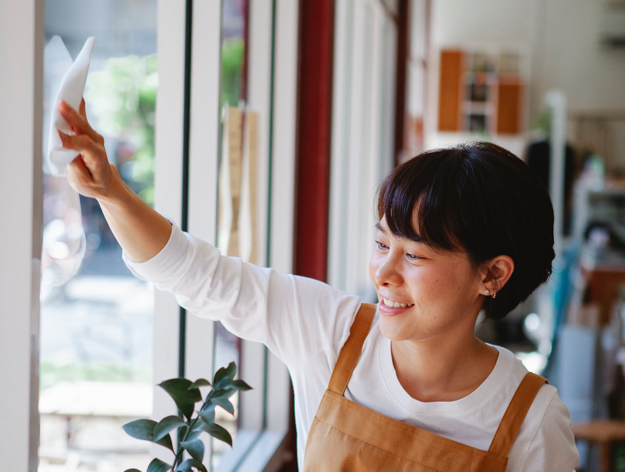about-02 Smiling woman in apron wipes glass window at a small business. Indoor shot.